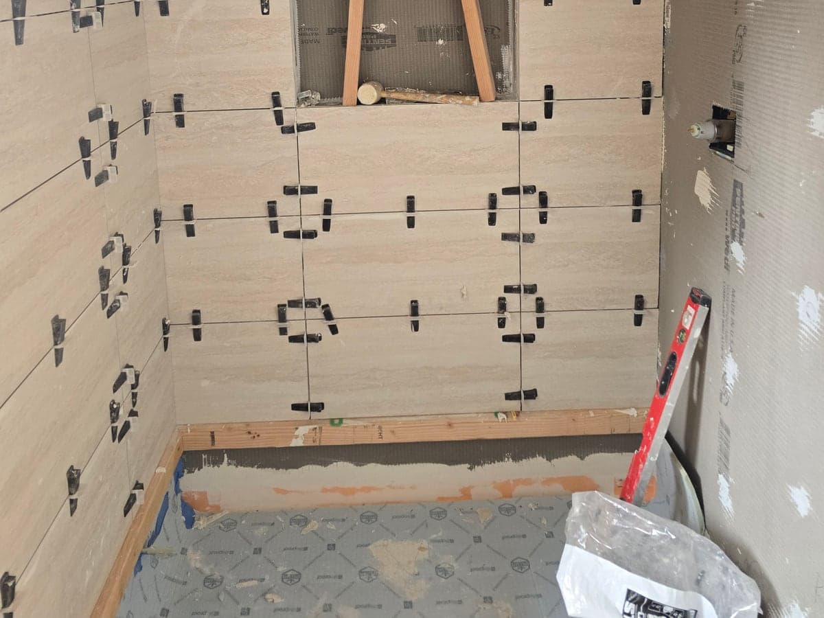 Large-format shower wall tile in progress with leveling clips, spacers, and a recessed niche.