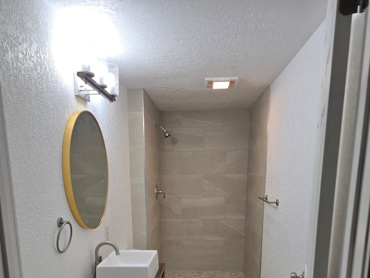 Completed compact bathroom with a tiled shower, wood vanity, white vessel sink, and round mirror.