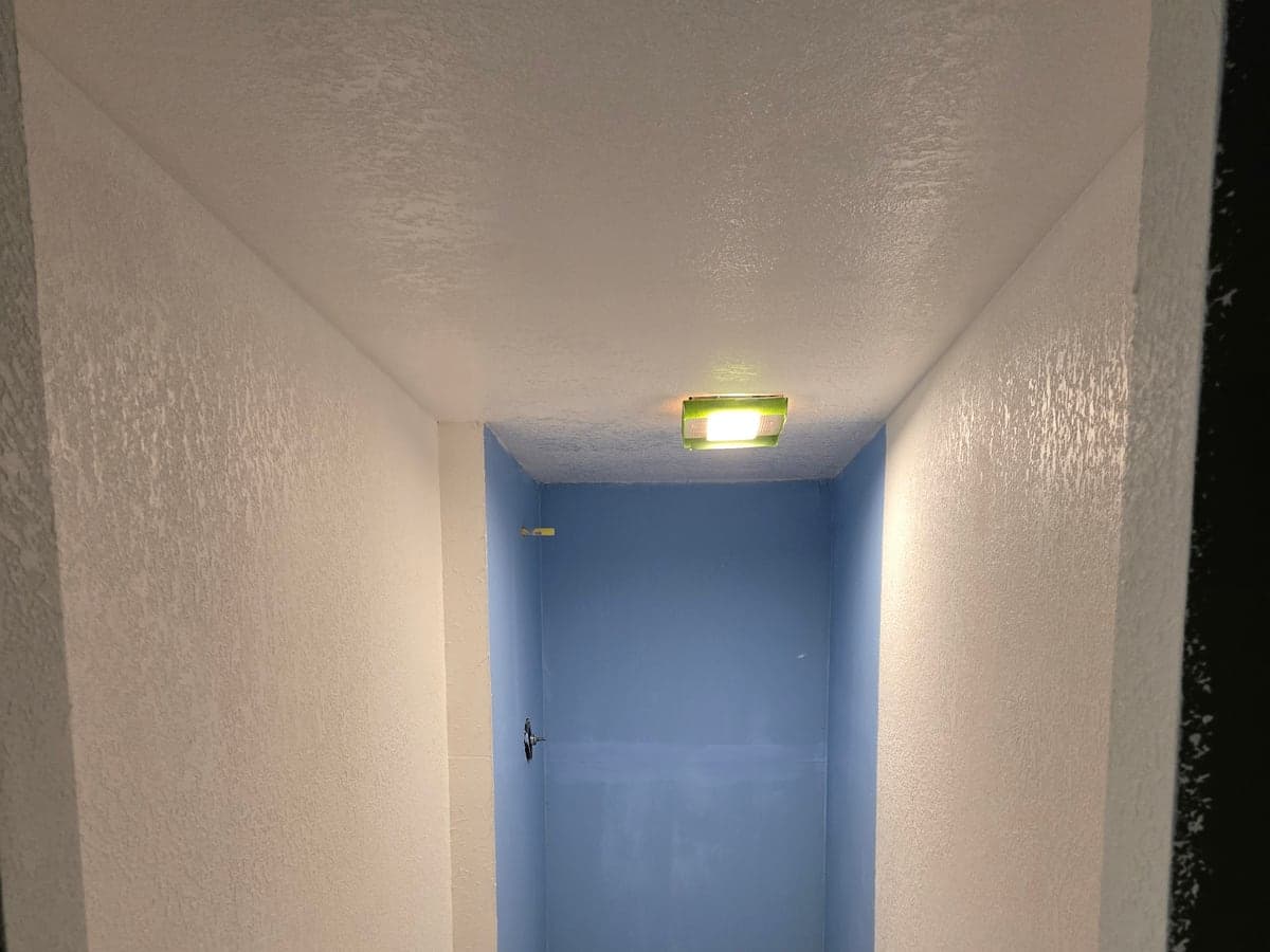 Unfinished bathroom alcove with blue-painted shower walls, a bare floor, and construction tools.