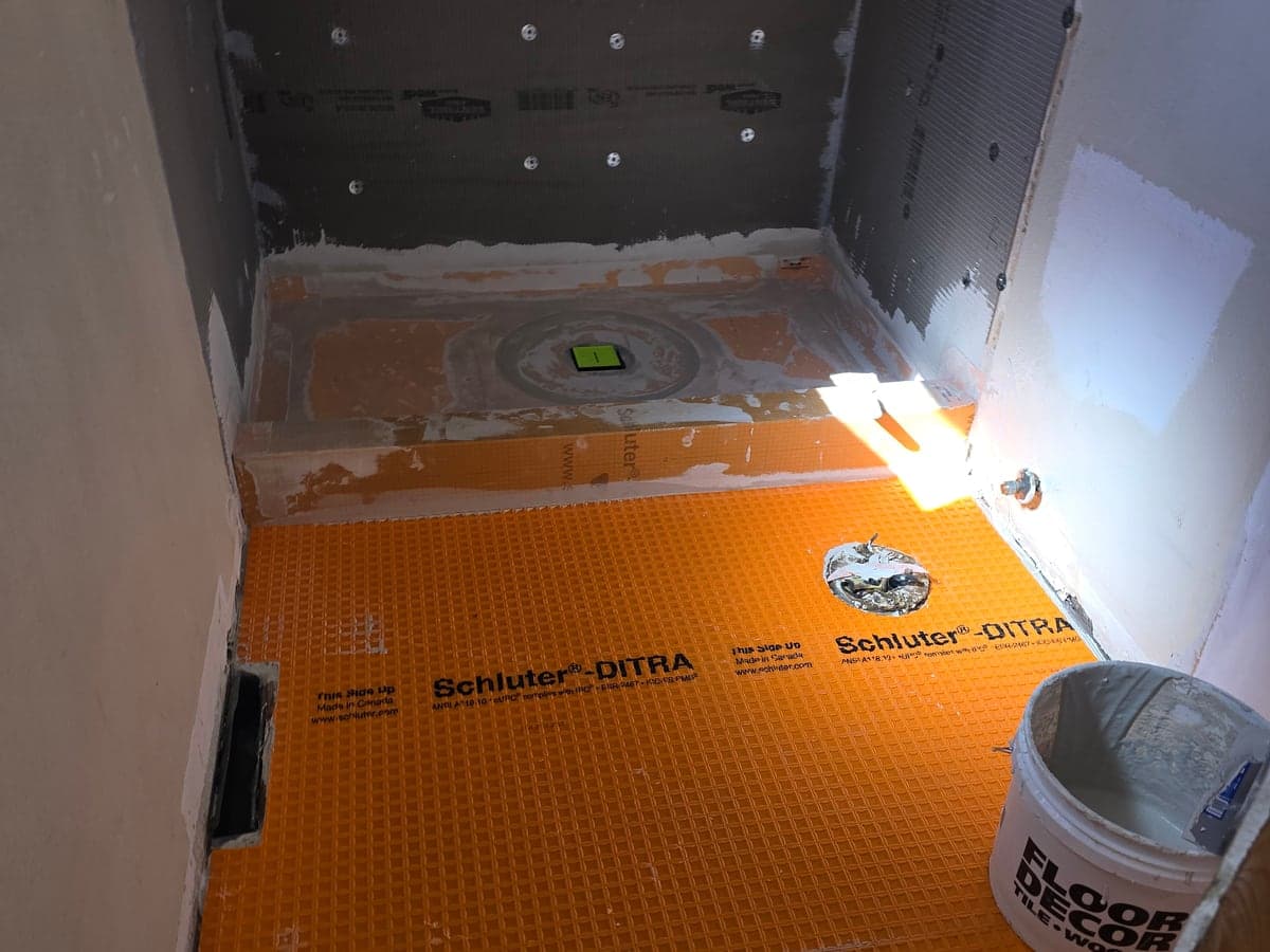 Bathroom floor under construction with a shower drain, waterproofing membrane, and unfinished walls.